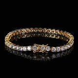 18K gold plated iced out tennis chain bracelet shown in a round hero shot on black reflective surface, single row of round cut cubic zirconia stones, hip hop bling jewelry for men and women