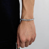 White gold plated cubic zirconia tennis chain bracelet on female wrist with black clothing against white background, everyday iced out tennis bracelet for women