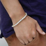 White gold plated cubic zirconia tennis chain bracelet worn on wrist with purple shirt and brown pants, iced out everyday bling bracelet for casual streetwear styling