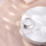 Green moissanite ring styled on hand against soft neutral backdrop